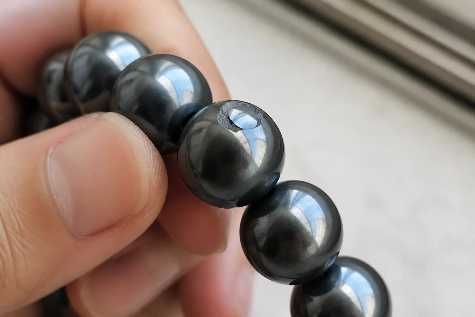 Close inspection of a chipped hematite bead on a bracelet with the damaged edge visible