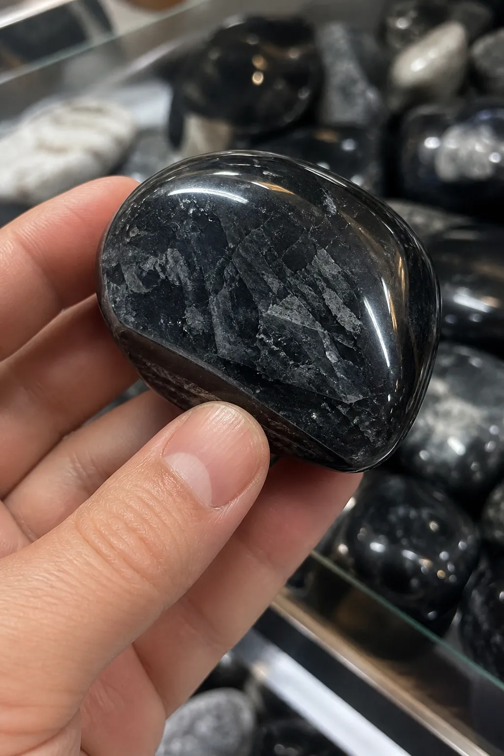 A hand checking a dark polished stone under bright light to compare metallic sheen, glassy surface, and existing edges