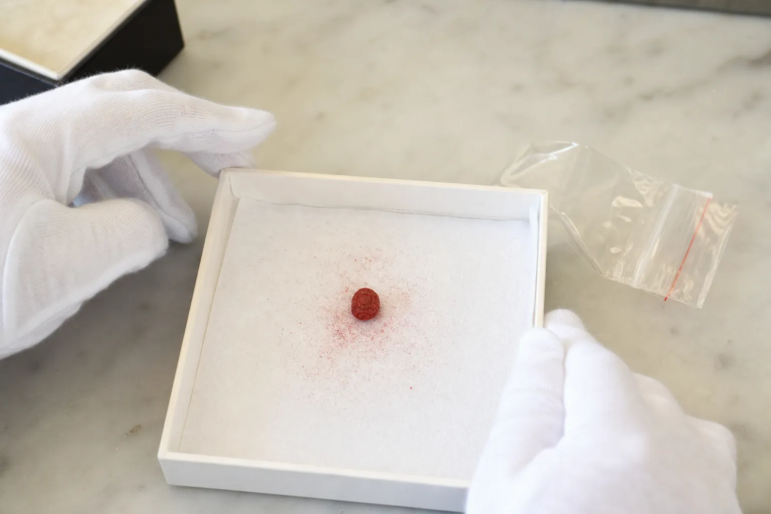 A powdery red cinnabar-labeled bead contained on a clean tray for low-disturbance inspection