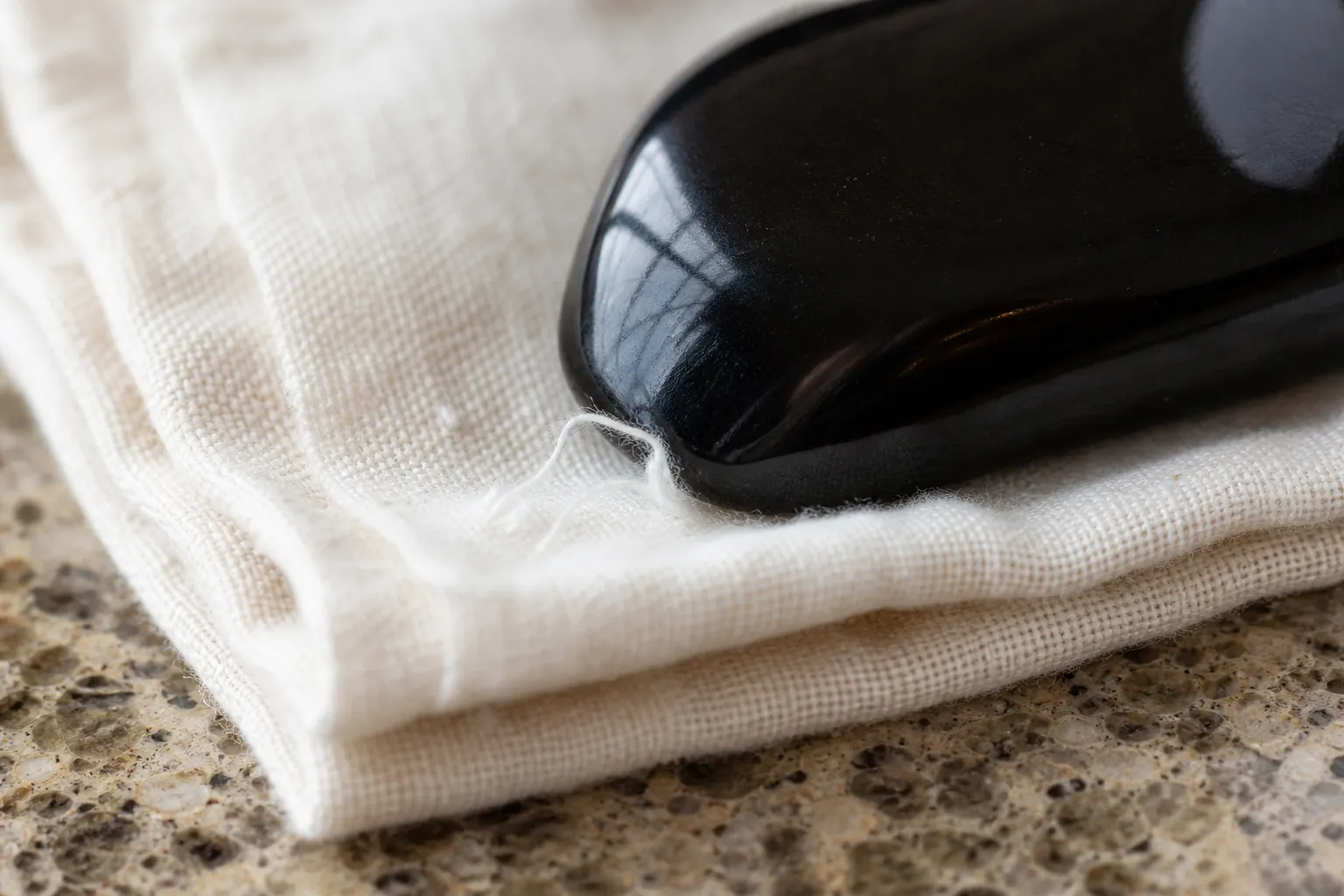 A polished obsidian stone being tested against soft cloth to check for snagging edges