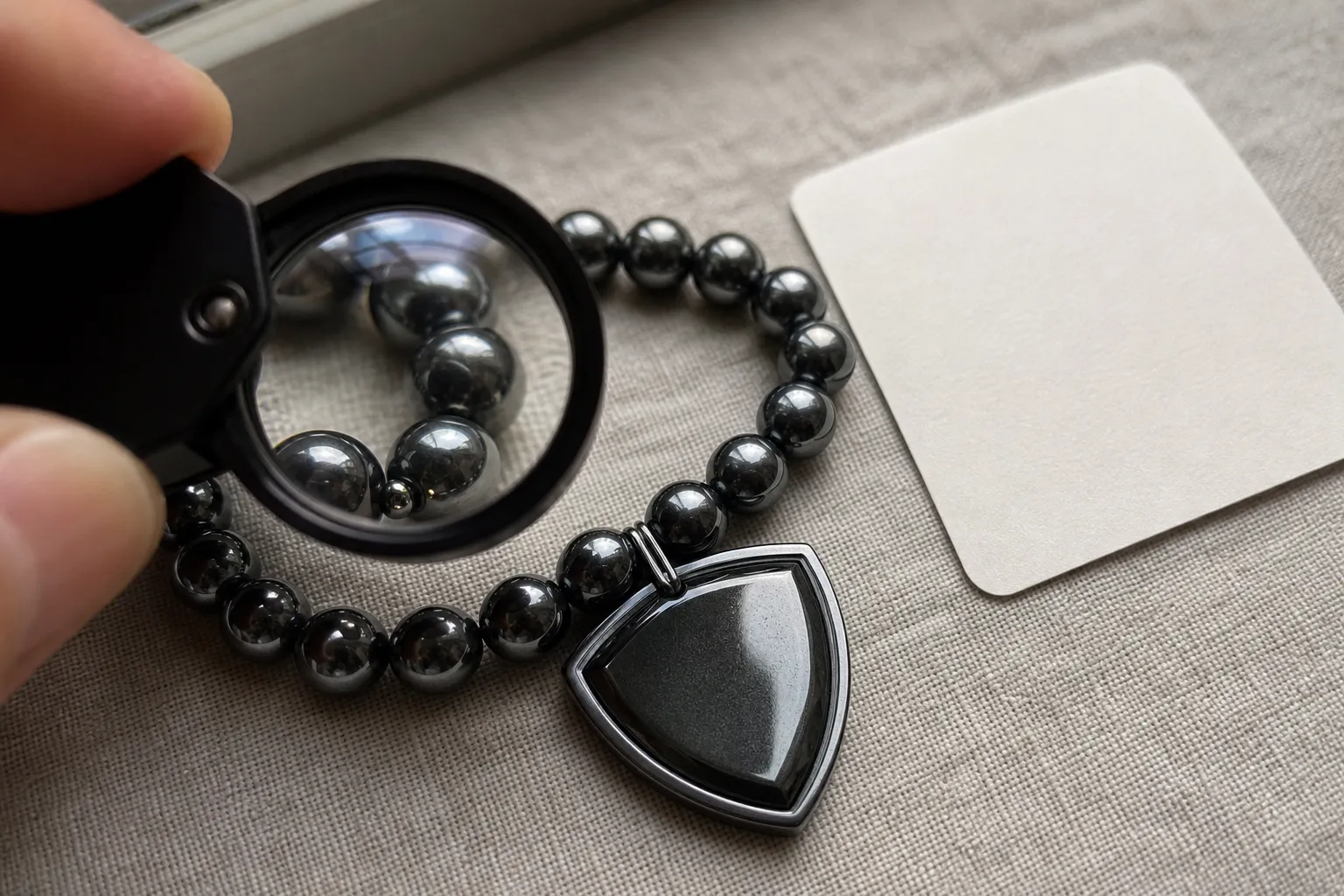 Close inspection of dark metallic hematite beads and a shield-like charm to compare wording with visible form