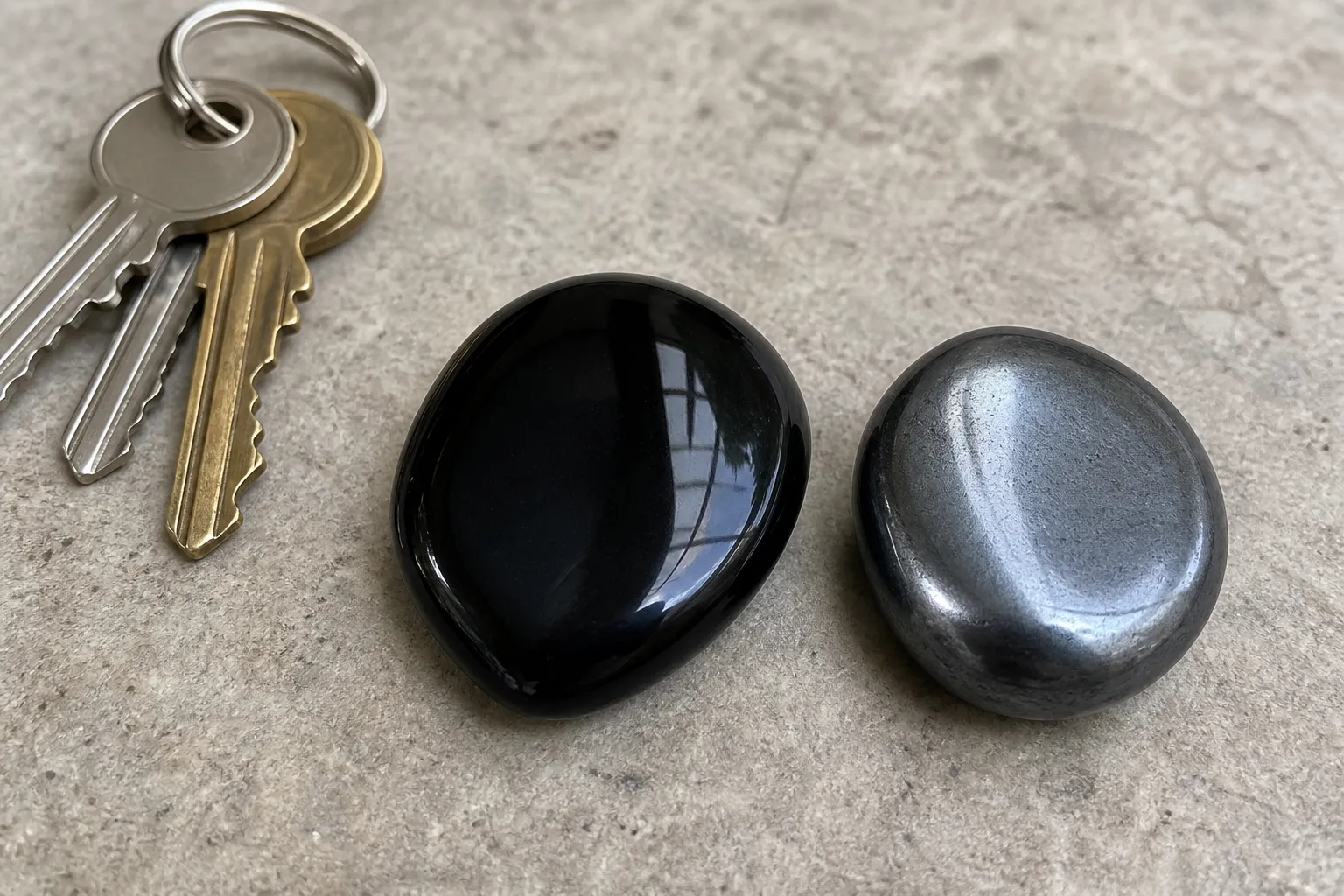 A polished obsidian pocket stone and a polished hematite pocket stone placed beside keys for everyday carry comparison