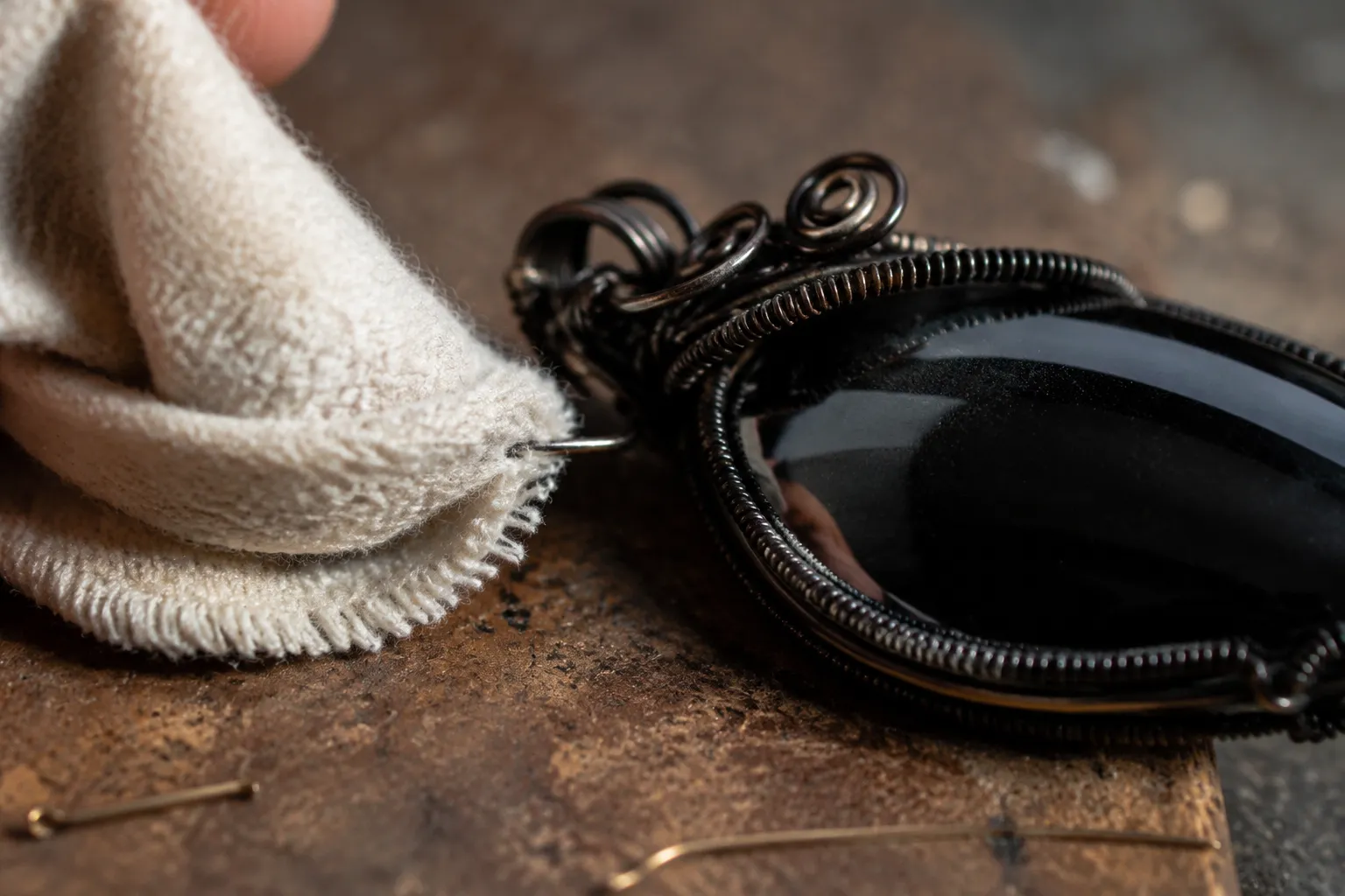 Soft cloth checking whether an obsidian pendant edge or wire end catches during a light inspection