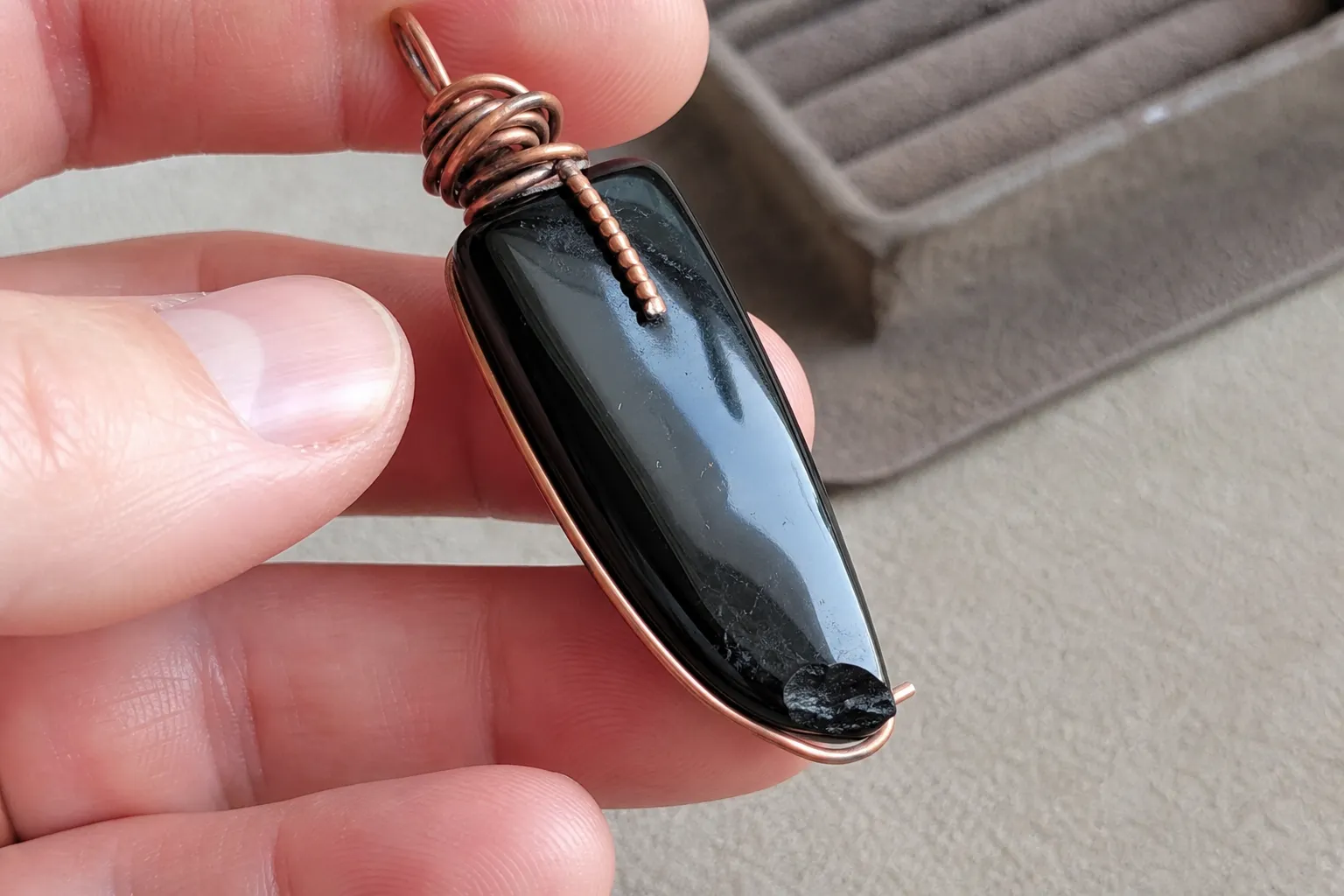 Close inspection of an obsidian pendant edge and wire wrap before wearing it against skin