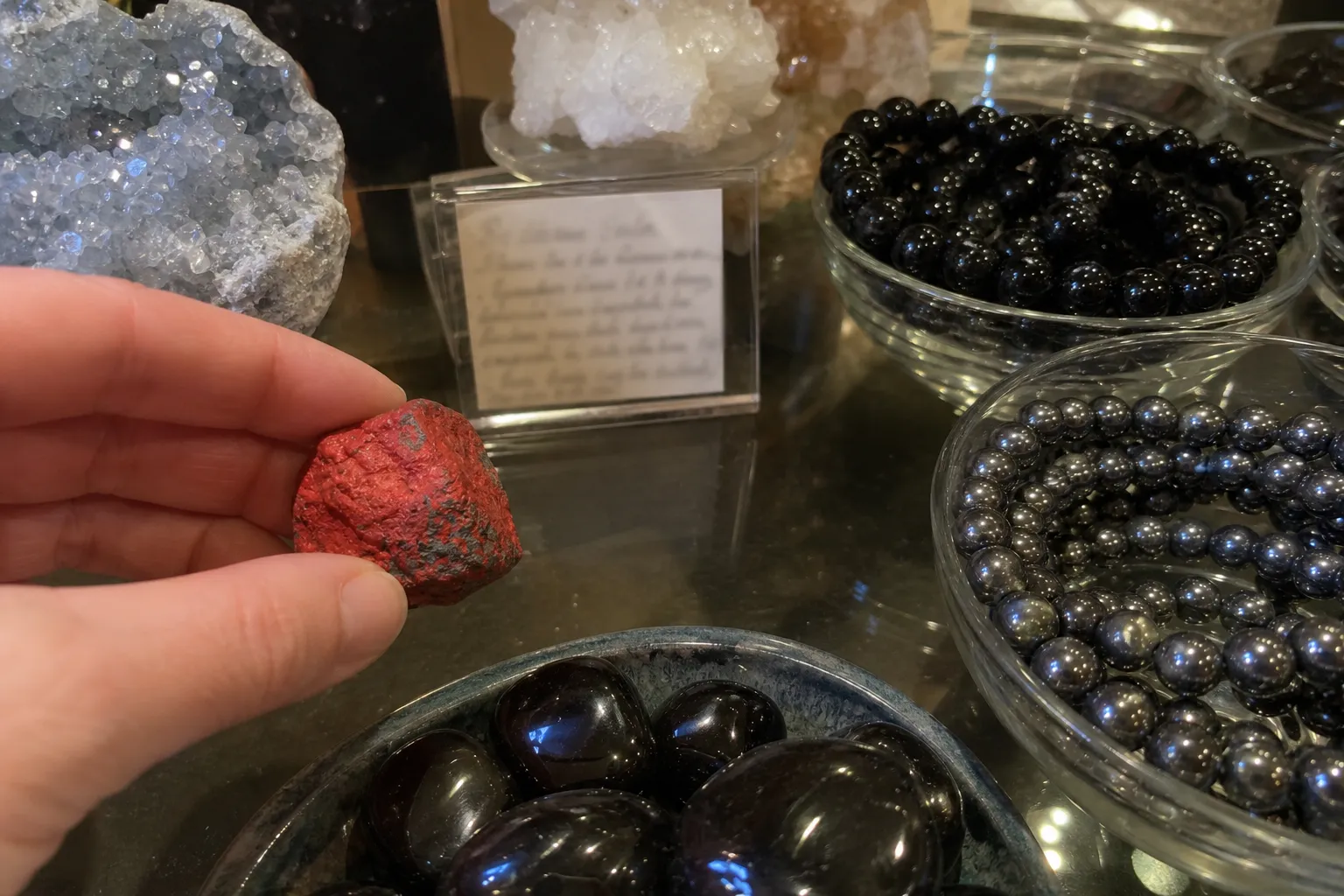 A careful handling note beside a red cinnabar specimen, polished obsidian, and hematite beads during a crystal comparison