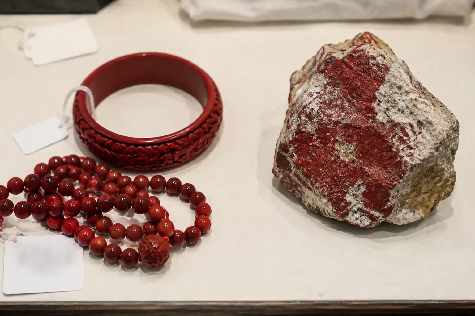 Red carved cinnabar style jewelry beside a rough cinnabar specimen for material comparison